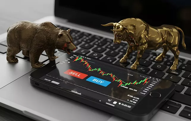 Bull and bear figurines on a laptop keyboard next to a smartphone showing a trading app