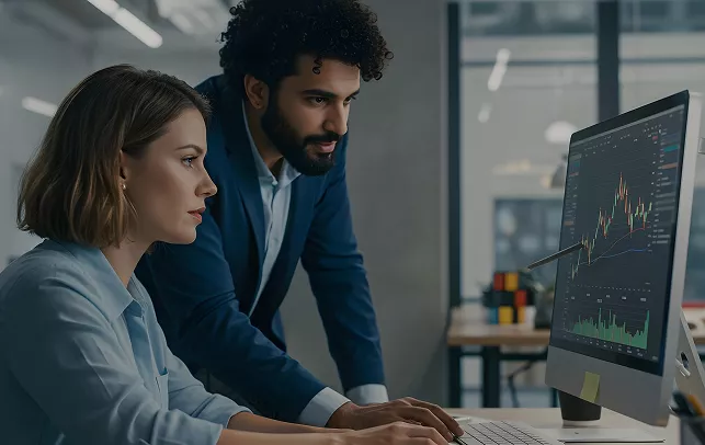 Two colleagues analyzing financial charts on a desktop monitor